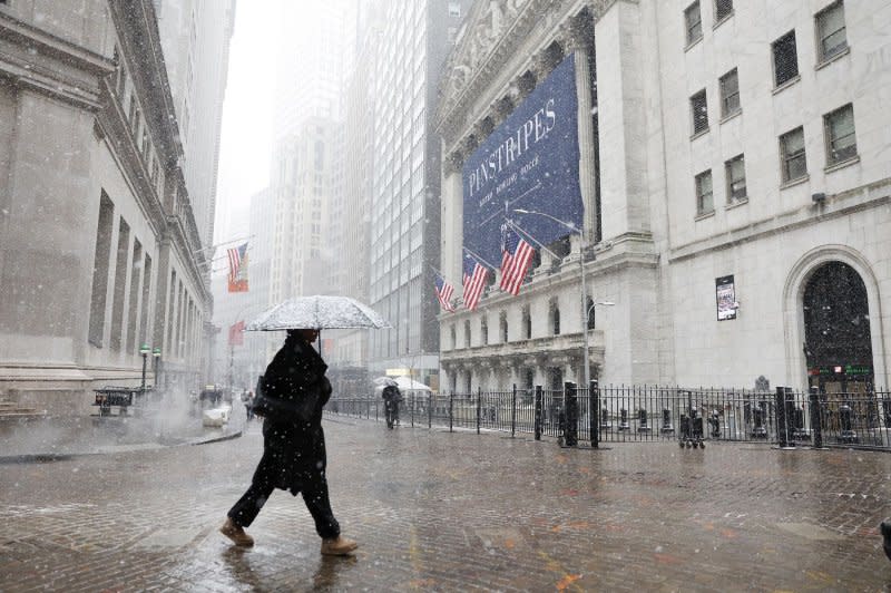 A pedestrian holding an umbrella walks past the New York Stock Exchange as snow falls accompanied by cold temperatures on Wall Street on Friday. Photo by John Angelillo/UPI