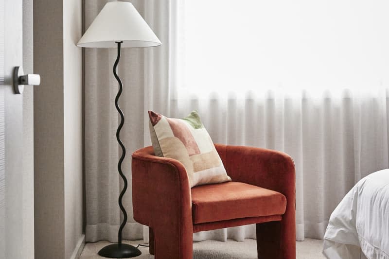 Photography detail of a rust coloured velvet armchair and a wiggly squiggle lamp in the corner of a bedroom.