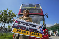 A passenger poses for a photo in front of a double-decker bus she got on board, in Hong Kong, Saturday, Oct. 16, 2021. Travel-starved, sleep-deprived residents might find a new Hong Kong bus tour to be a snooze. The 76-kilometer (47-mile), five-hour ride on a regular double-decker bus around the territory is meant to appeal to people who are easily lulled asleep by long rides. It was inspired by the tendency of tired commuters to fall asleep on public transit. The banner reads: "The first in Hong Kong! Snooze bus tour." (AP Photo/Kin Cheung)