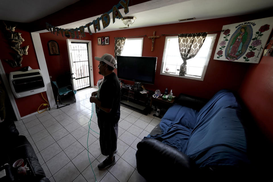 Freddy Fernandez is tethered to an oxygen concentrator as he stands in the living room of his home Friday, June 10, 2022, in Carthage, Mo. After contracting COVID-19 in August 2021, Fernandez spent months hooked up to a respirator and an ECMO machine before coming home in February 2022 to begin his long recovery from the disease. (AP Photo/Charlie Riedel)
