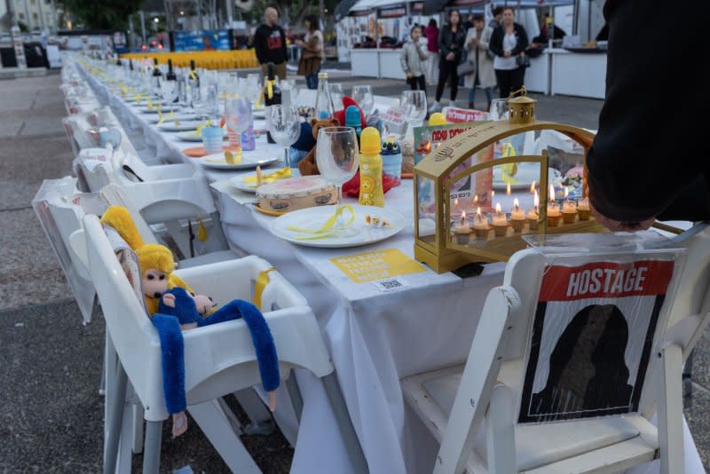 A Hanukkiah candelabra is lit with candles on the night before the Jewish holiday of Hanukkah, the Festival of Lights, finishes at the head of an empty table set for the Israeli hostages held in the Gaza Strip on "Hostages Square" at the Tel Aviv Museum in Tel Aviv, Israel on Wednesday. Photo by Jim Hollander/UPI