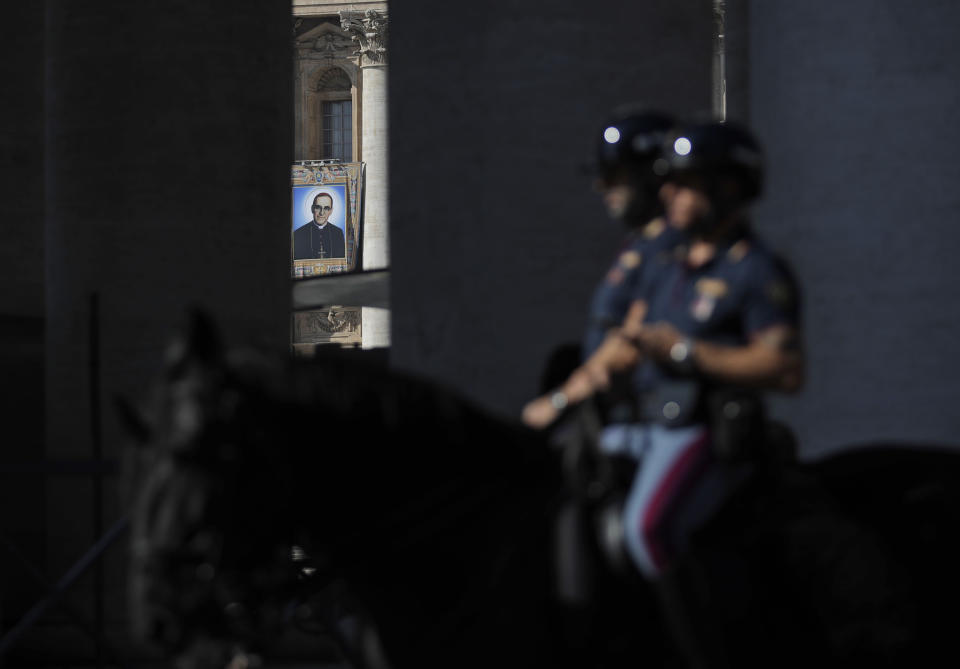 FILE - In this Friday, Oct. 12, 2018, horse mounted police ride past the tapestry of martyred Roman Catholic Archbishop Oscar Romero hanging from a balcony of the facade of St. Peter's Basilica at the Vatican. Pope Francis will canonize two of the most important and contested figures of the 20th-century Catholic Church, declaring Pope Paul VI and the martyred Salvadoran Archbishop Oscar Romero as models of saintliness for the faithful today. Sunday's ceremony is likely to be emotional for Francis, since he was greatly influenced by both men and privately told confidantes he wanted them made saints during his papacy. (AP Photo/Alessandra Tarantino, File)