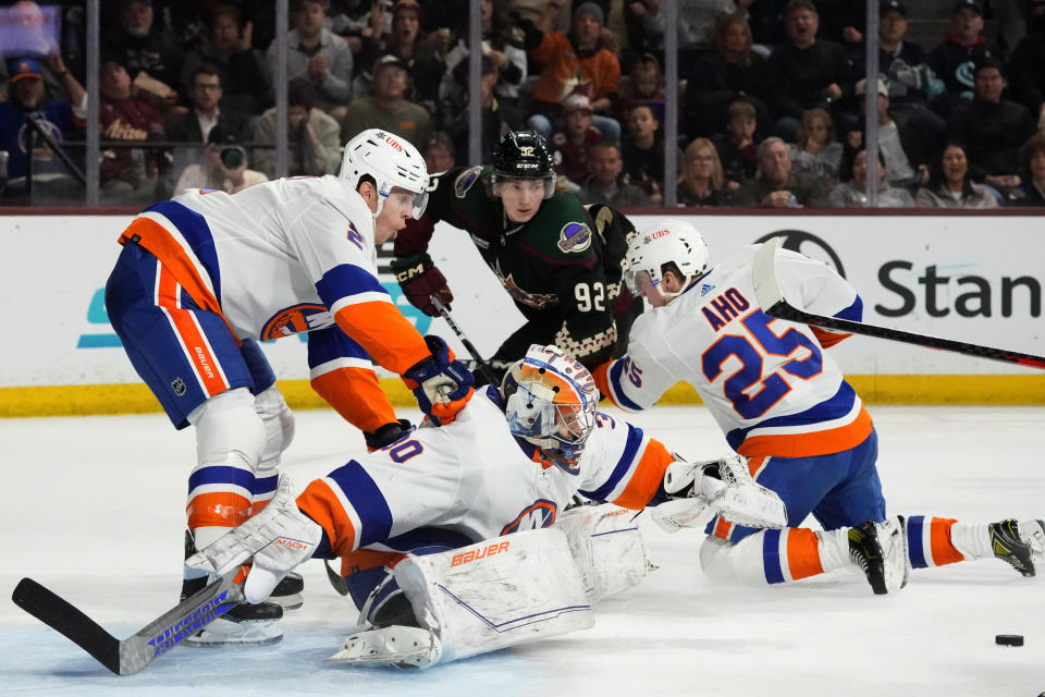New York Islanders goaltender Ilya Sorokin, center, makes a save on a shot as he gets help from defensemen Mike Reilly, left, and Sebastian Aho (25), while Arizona Coyotes center Logan Cooley (92) watches during the third period of an NHL hockey game Thursday, Jan. 4, 2024, in Tempe, Ariz. The Islanders won 5-1. (AP Photo/Ross D. Franklin)