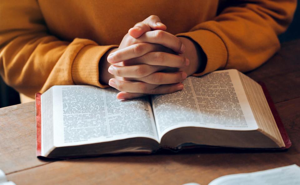 hands clasped together on her Bible praying to god. believe in goodness. Holding hands in prayer on a wooden table. Christian life crisis prayer to god.