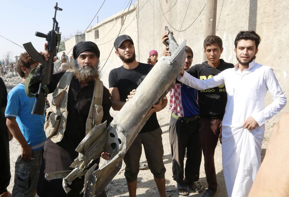 An Islamic State militant (L) stands next to residents as they hold pieces of wreckage from a Syrian war plane after it crashed in Raqqa, in northeast Syria September 16, 2014. The Syrian war plane crashed near the Islamic State-controlled city of Raqqa on Tuesday, a resident said, and a group that tracks violence in the war said a number of people had been wounded on the ground. REUTERS/Stringer (SYRIA - Tags: POLITICS CIVIL UNREST CONFLICT TRANSPORT TPX IMAGES OF THE DAY)