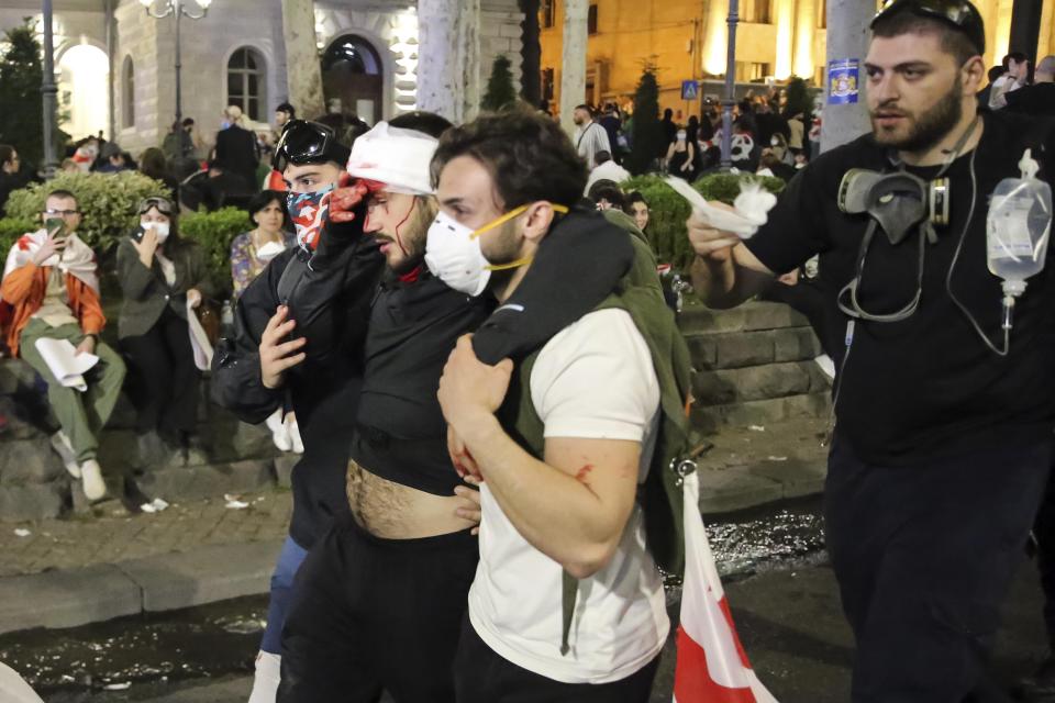 Demonstrators help their comrade being wounded in clashes with police during an opposition protest against "the Russian law" near the Parliament building in Tbilisi, Georgia, on Thursday, May 2, 2024. Protesters denounce the bill as "the Russian law" because Moscow uses similar legislation to stigmatize independent news media and organizations critical of the Kremlin. (AP Photo/Zurab Tsertsvadze)