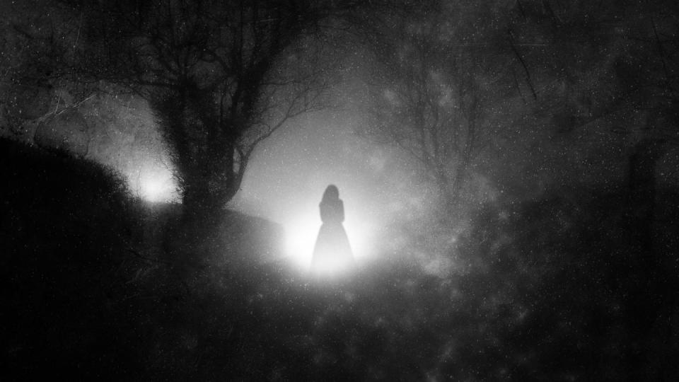 a country lane, on a foggy night with a ghostly woman in a dress in front of glowing lights with a grunge, blurred, vintage edit