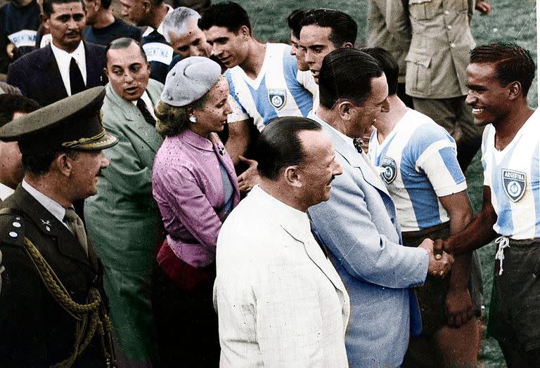 El presidente Juan Domingo Perón y su esposa, Eva Duarte, saludan al plantel argentino que ganó la medalla de oro en los Juegos Panamericanos realizados en Buenos Aires, en 1951. En primer plano, de saco blanco, aparece Carlos Paillot, presidente de Racing. De verde, detrás de la primera dama, está el ministro de Hacienda, Luis Cereijo.