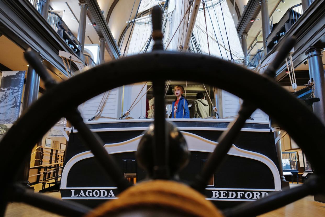 A young boy takes a look out of the stern opening of the Lagoda one half scale model of a whale ship at the Whaling Museum in New Bedford as seen through a helm on display.