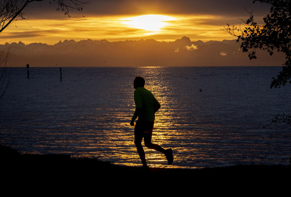 A man runs along the lake of Constance with the Swiss Alps in background during sunrise in Constance, Germany, Thursday, Nov. 14, 2019. (AP Photo/Michael Probst)