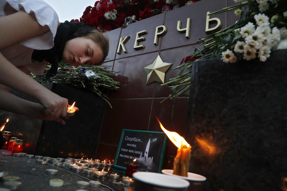A girl lights a candle in memory of the victims of Wednesday's attack on a vocational college in Kerch, Crimea, at the memorial stone with the word Kerch in the Alexander Garden near the Kremlin, Moscow, Russia, Thursday, Oct. 18, 2018. A top official in Crimea says authorities are searching for a possible accomplice of the student whose shooting-and-bomb attack on his vocational school killed 20 people and wounded more than 50 others. (AP Photo/Pavel Golovkin)
