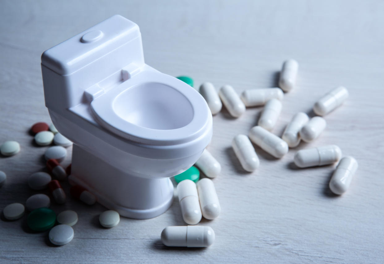 A tiny plastic toilet is surrounded by pills and tablets.