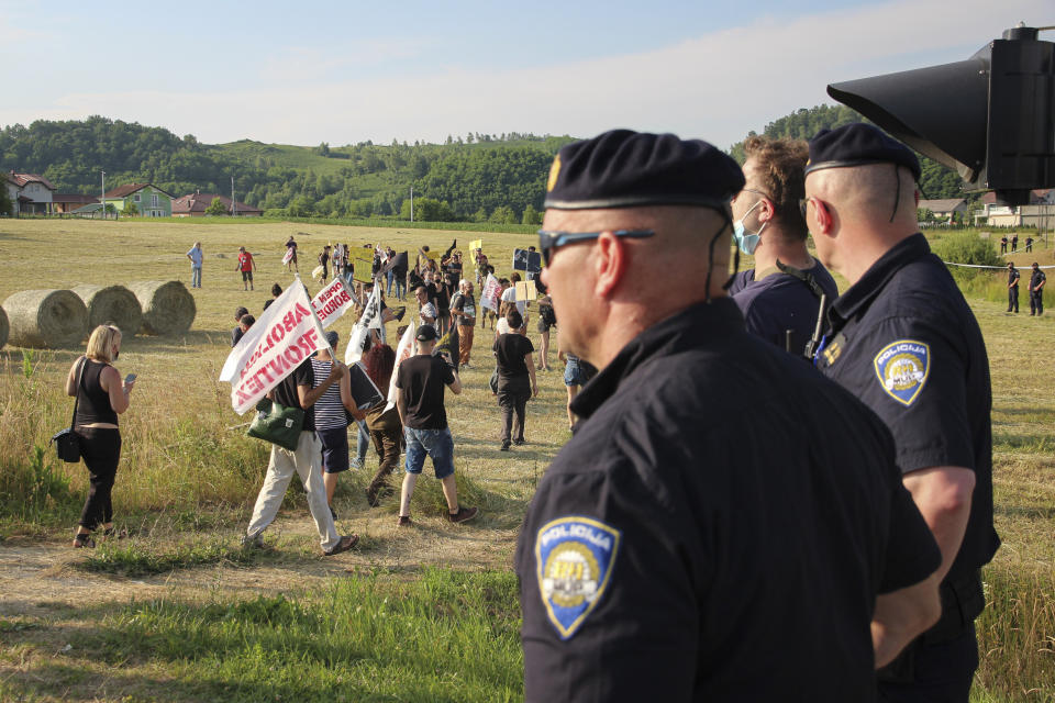 Croatian police officers stand as people walk with banners during a protest against the violent pushbacks of migrants, allegedly conducted by Croatian police, near the border crossing between Croatia and Bosnia Herzegovina in Maljevac, Croatia, Saturday, June 19, 2021. More than one hundred members of human rights NGO's, mostly from Italy, but also from Germany, Austria, Spain and Slovenia blocked the border traffic for about two hours protesting demanding a stop of all deportation of migrants, and cancellation of EU's Frontex operations at borders, preventing migrants from traveling. (AP Photo/Edo Zulic)