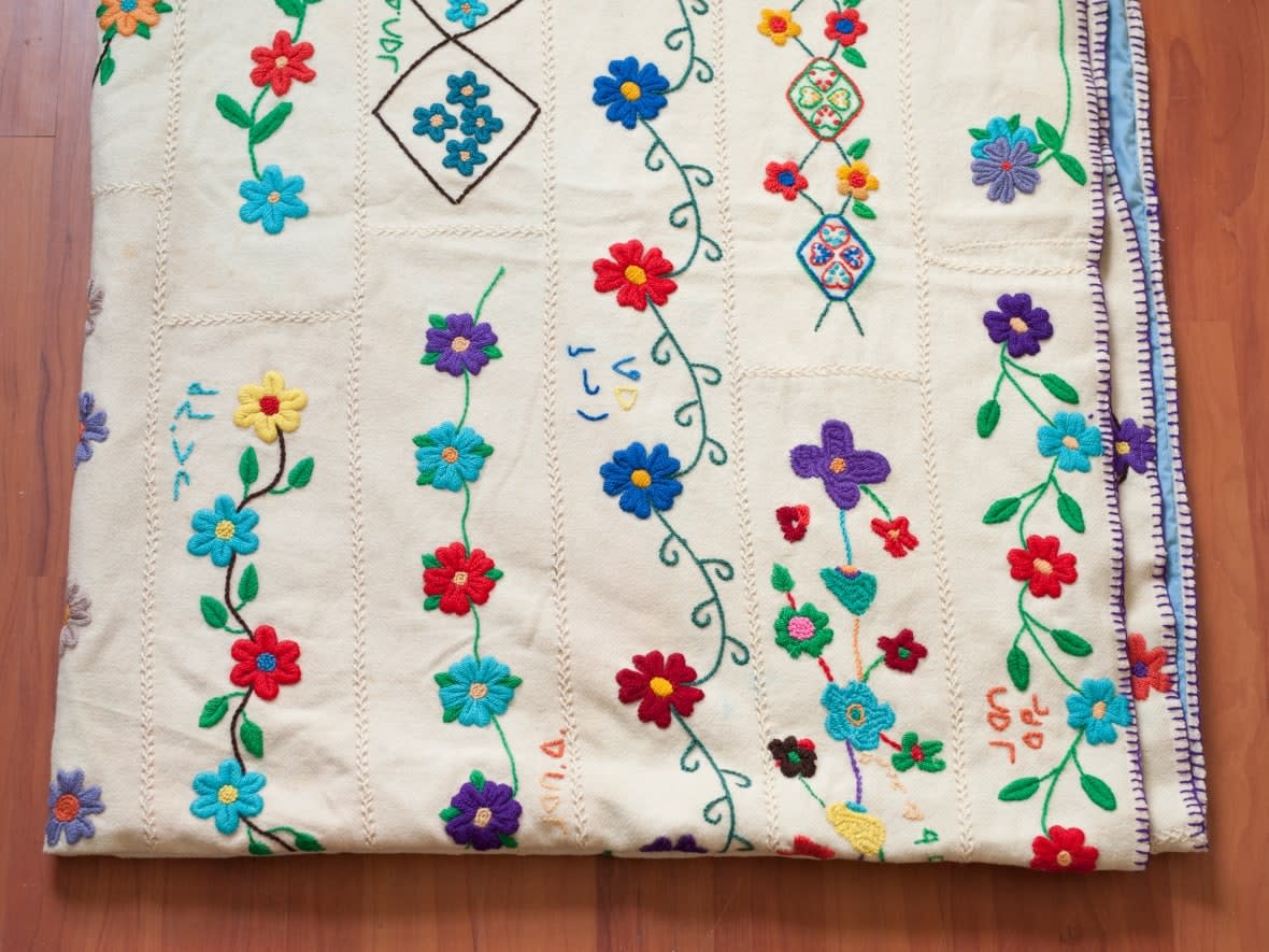 This blanket made by women in Taloyoak in the 1970s and brought back to the community last year went missing on its return south.  The white duffle blanket was made of sampler pieces of embroidery sewn together and lined with a blue sheet. Names on the sampler pieces are: Eeteeklook, Taleerak, Qayaut, Philamena Tootalik, Mary Napachie, Oblurak, Seta, Arnaluaq, Oktookie, Mosie Jako, Eeteemunga, Anouyok Aiyaut, Lena Kokeak, Teresa Totalik, Marangnaq, Quyuk Poodlat, Maudie Iqilik, Mary Omingmuk. (Submitted by Pitquhirnikkut Ilihautiniq/ Kitikmeot Heritage Society - image credit)