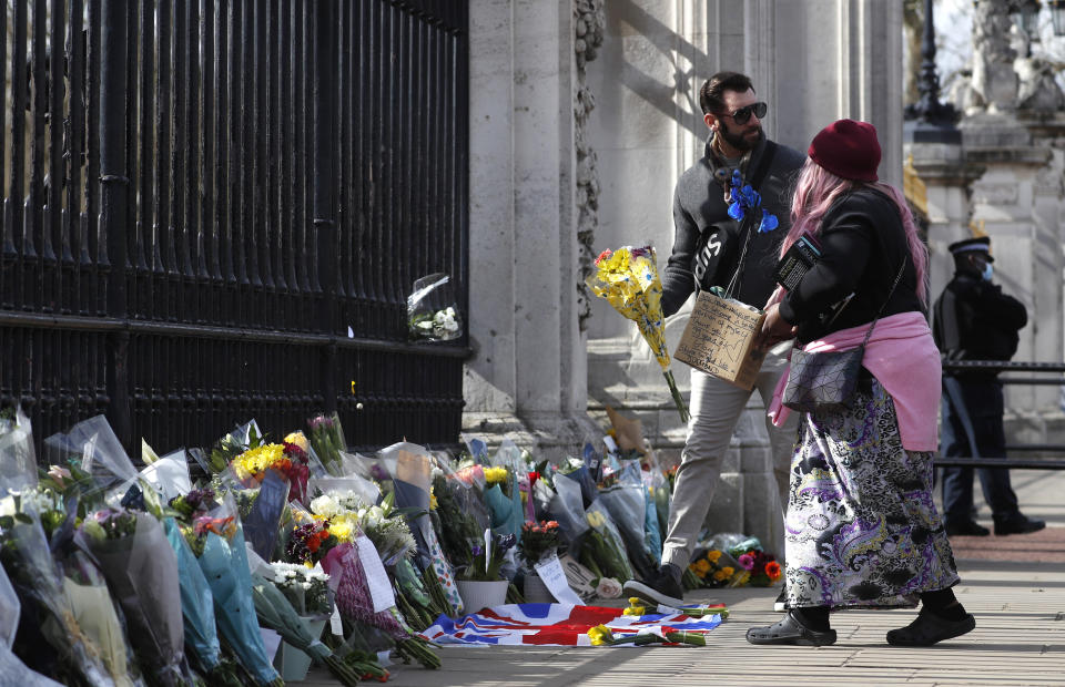 A woman prepares to lay a bouquet of flowers in a box with a message near the front of the gate at Buckingham Palace in London, Friday, April 9, 2021. Buckingham Palace officials say Prince Philip, the husband of Queen Elizabeth II, has died. He was 99. Box reads 'you have inspired me to become a better version of myself. Thank you, 99 years of glory. Shine bright like a diamond.' (AP Photo/Alastair Grant)