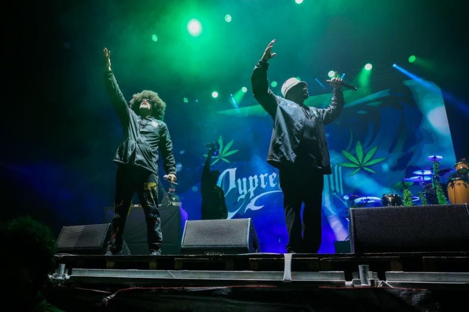B-Real and Sen Dog, the two lead rappers of Cypress Hill, raise their arms in the air during a performance.