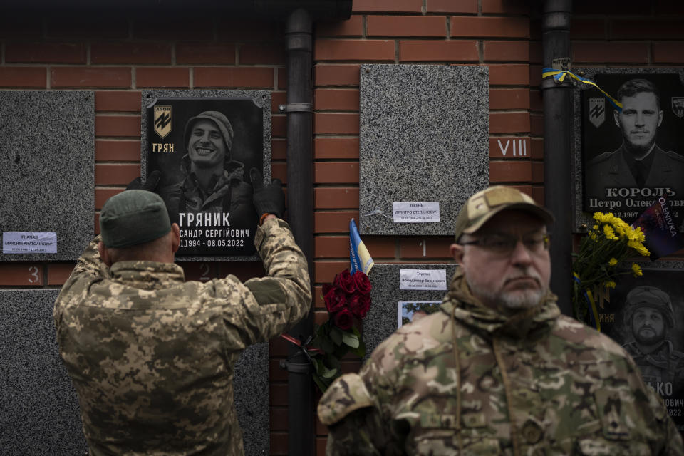 A colleague hangs up a memorial picture on the grave of Ukrainian soldier Oleksandr Hrianyk in Kyiv, Ukraine, Saturday, Oct. 28, 2023. Hrianyk died in battle in May 2022 in the city of Mariupol, but was only cremated recently after his remains were found and identified. (AP Photo/Bram Janssen)