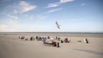 In this Saturday, May 16, 2020 photo a seagull flies over a small number of beach chairs on the island Spiekeroog, Germany. Germany's states, which determine their own coronavirus-related restrictions, have begun loosening lockdown rules to allow domestic tourists to return. (Sina Schuldt/dpa via AP)