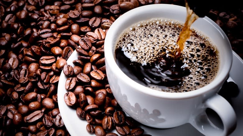 Pouring coffee into a white ceramic mug next to coffee beans