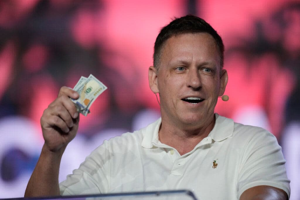 Peter Thiel, co-founder of PayPal and Palantir, offers a pair of hundred dollar bills to attendees during a keynote address at the Bitcoin Conference, April 7, 2022, in Miami Beach, Fla.. (AP Photo/Rebecca Blackwell, File)