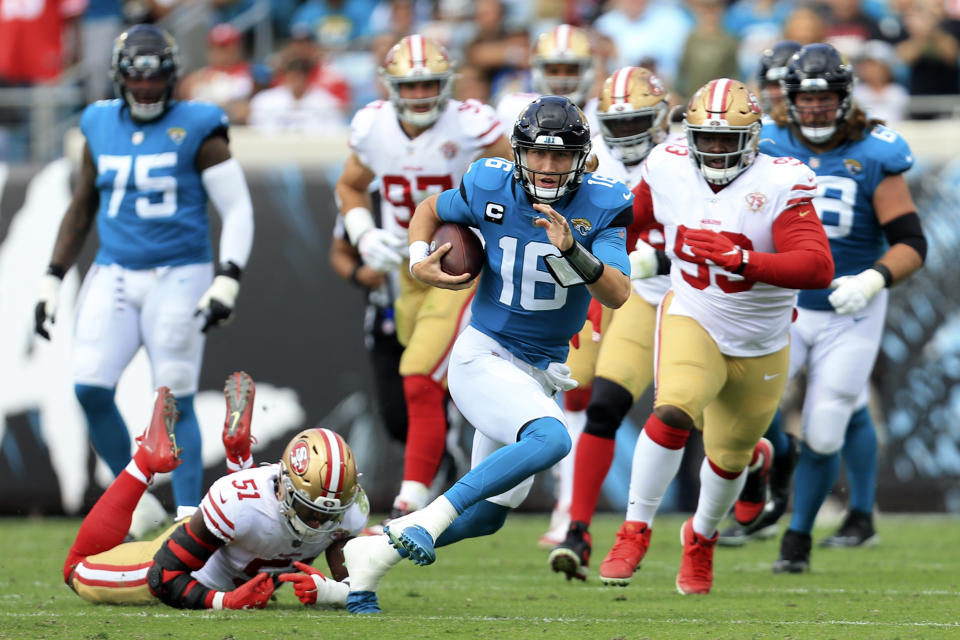 Jacksonville Jaguars quarterback Trevor Lawrence (16) scrambles for yardage as he gets away from San Francisco 49ers linebacker Azeez Al-Shaair (51) and defensive tackle D.J. Jones, right, during the first half of an NFL football game, Sunday, Nov. 21, 2021, in Jacksonville, Fla. (AP Photo/Matt Stamey)