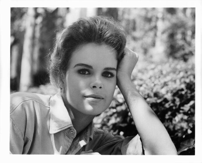 A black-and-white closeup shot of a young woman wearing a collared shirt and resting her head on her arm