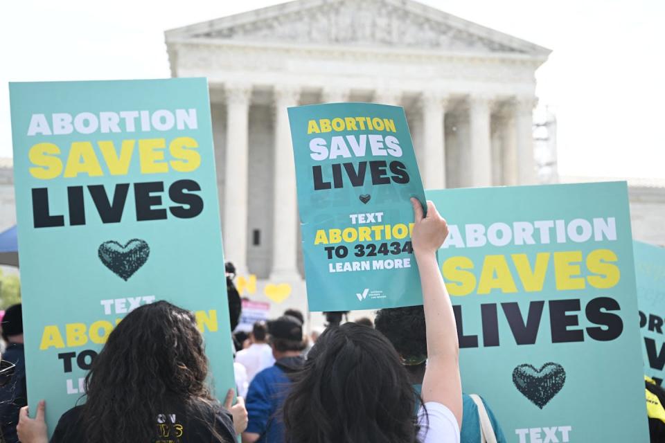 People hold signs that say 'Abortion saves lives' and face toward the Supreme Court on a grey day.