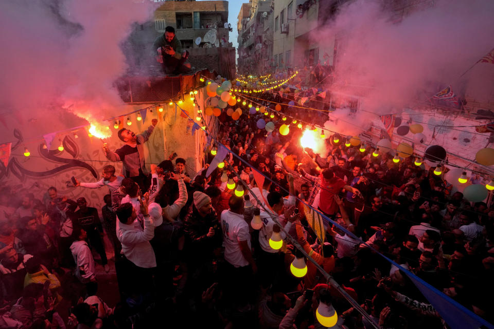 Residents of Ezbet Hamada in Cairo's El Matareya district light flares as the celebrate mass breakfast, "Iftar", the meal to end their fast at sunset, during the holy fasting month of Ramadan in Cairo, Monday, March 25, 2024. (AP Photo/Amr Nabil)