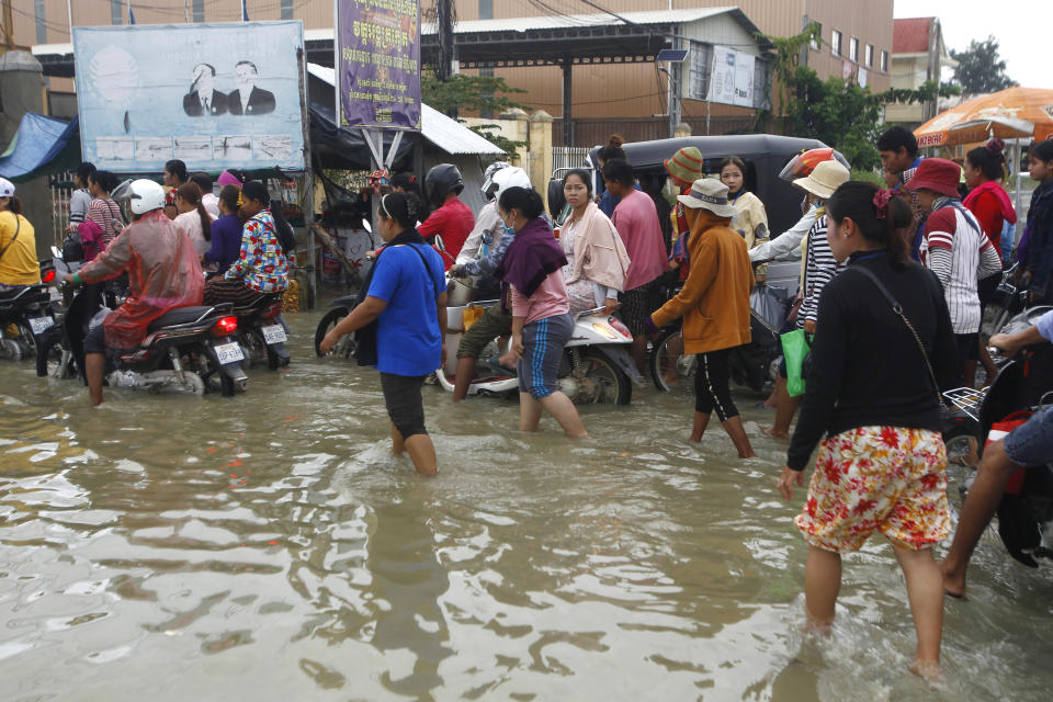 Garment workers going to work wade through flood waters following recent rains outside Phnom Penh, Cambodia, Wednesday, Oct. 14, 2020. A Cambodian disaster official said Wednesday that more than 10,000 people have been evacuated to the safety places after the tropical storm hit the country by causing the flash flood. (AP Photo/Heng Sinith)