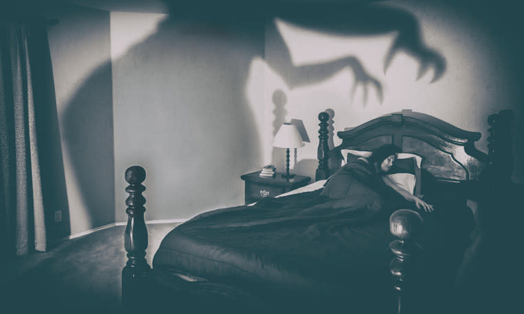 A shadow with claws on the wall over a sleeping woman