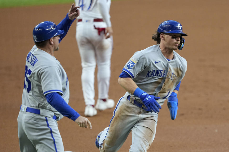 Kansas City Royals third base coach Vance Wilson, left, waves Bobby Witt Jr. home who scored on a fielding error by Texas Rangers right fielder Adolis Garcia in the first inning of a baseball game, April 10, 2023, in Arlington, Texas. (AP Photo/Tony Gutierrez)