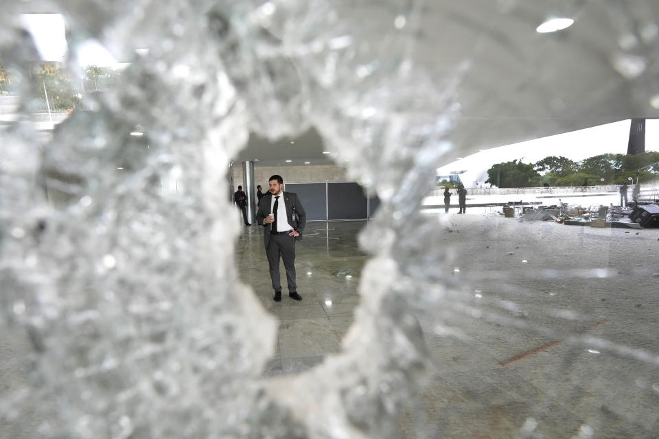 A worker stands on the other side of a broken window at Planalto Palace the day after the office of the president was stormed by supporters of Brazil's former President Jair Bolsonaro in Brasilia, Brazil, Monday, Jan. 9, 2023. The protesters also stormed Congress and the Supreme Court. (AP Photo/Eraldo Peres)
