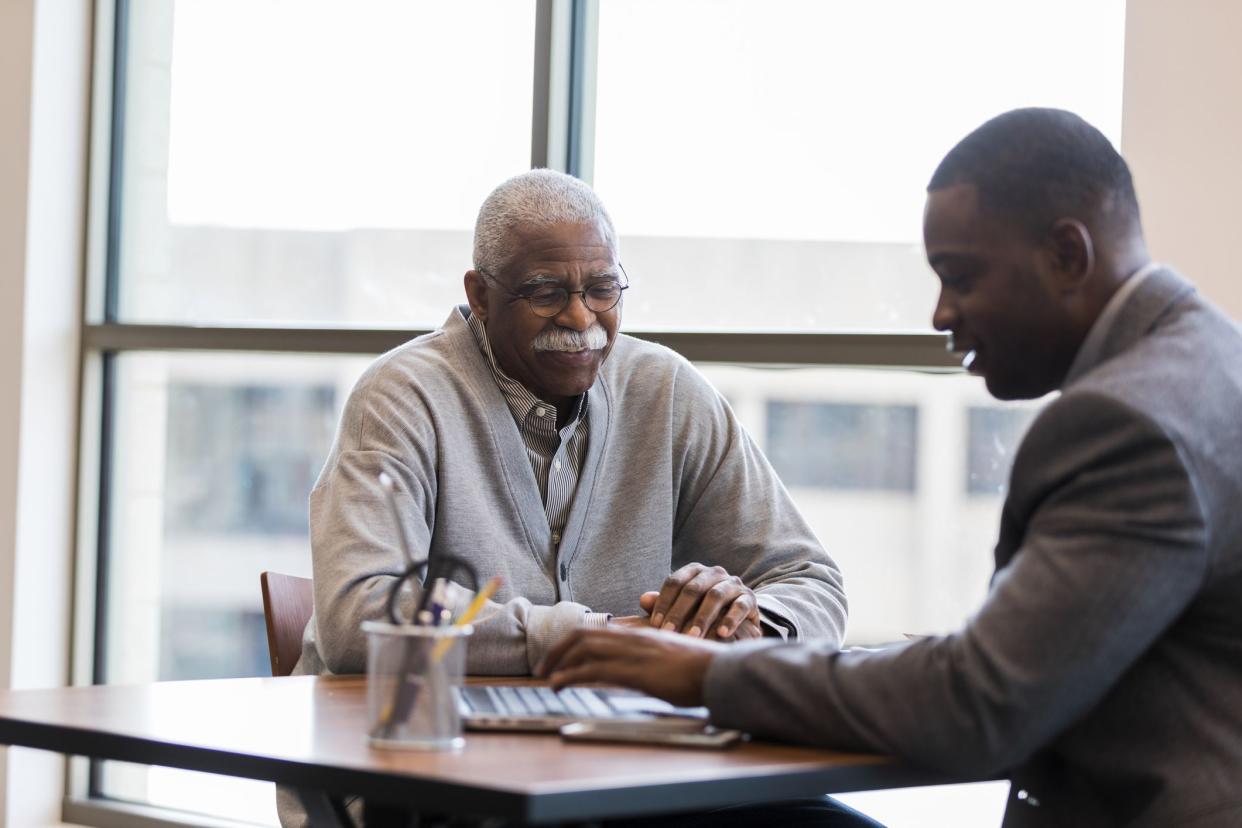 The mid adult loan officer patiently and cheerfully help sthe senior man find the best investment option for retirement savings.