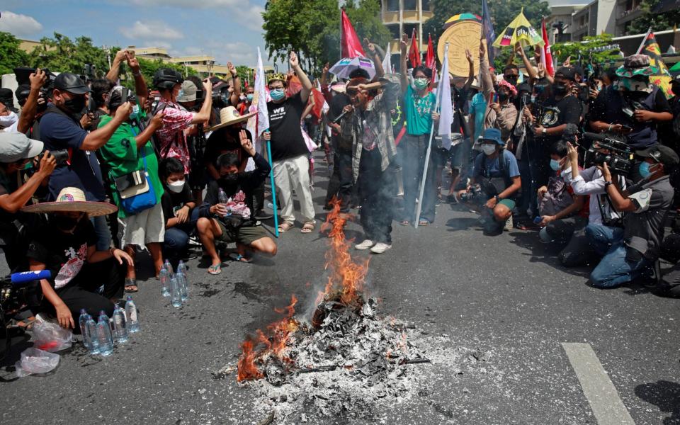 Protest leader Parit "Penguin" Chiwarak (with crown) shows the three-finger salute during a demonstration, as protesters set fire to a model of Democracy Monument, to mark the 89th anniversary of the abolition of absolute monarchy in Bangkok, Thailand, - Reuters