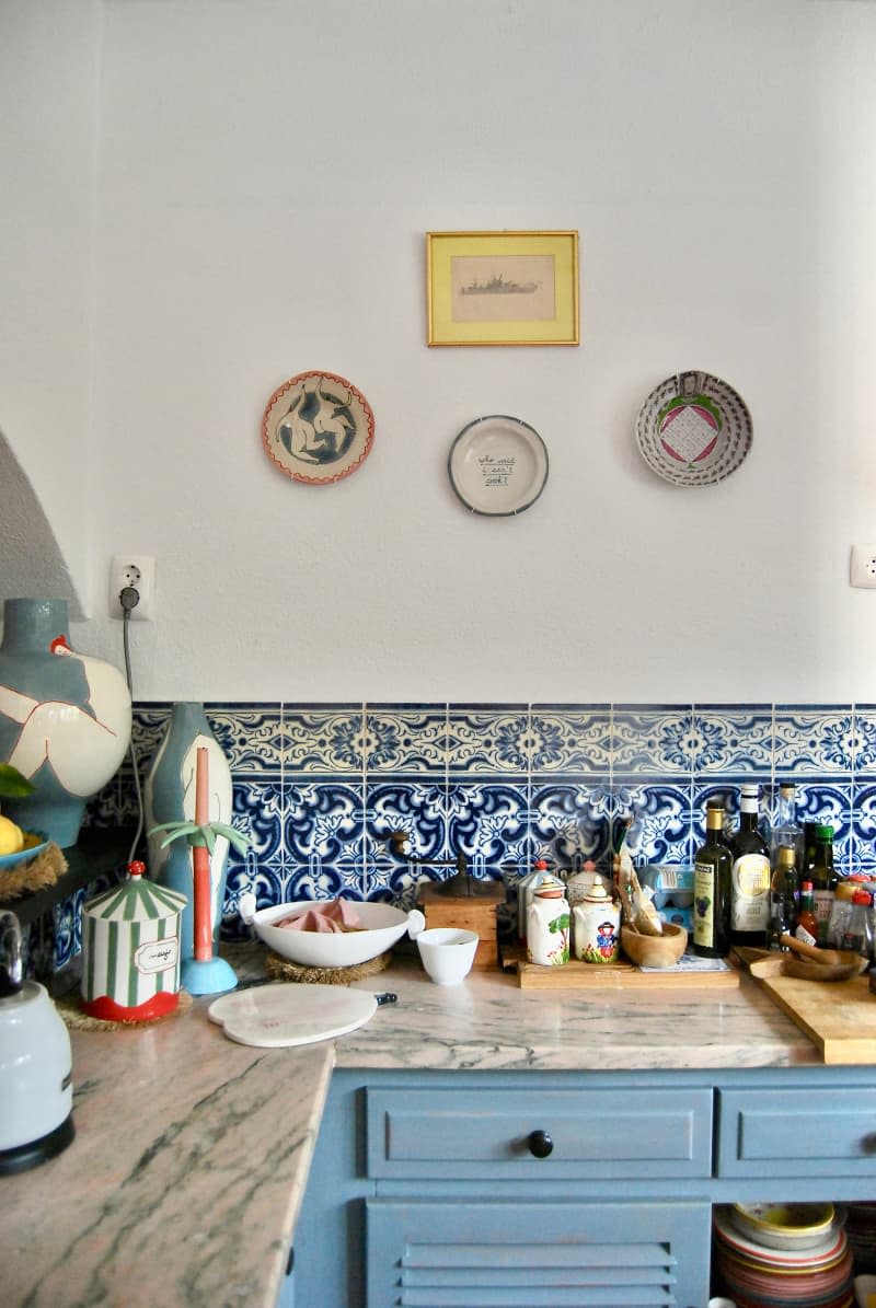 Marble countertops hold kitchen accessories in room with blue tiling and cabinets.