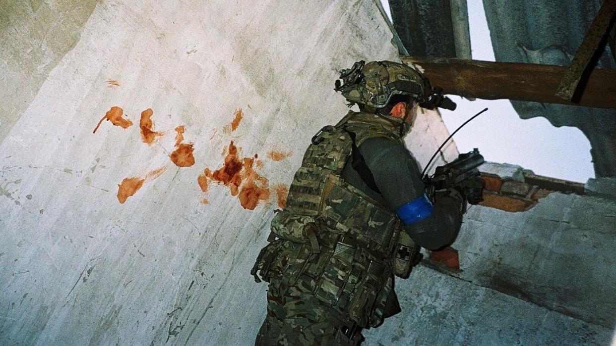 A soldier points a gun next to a blood-splattered wall