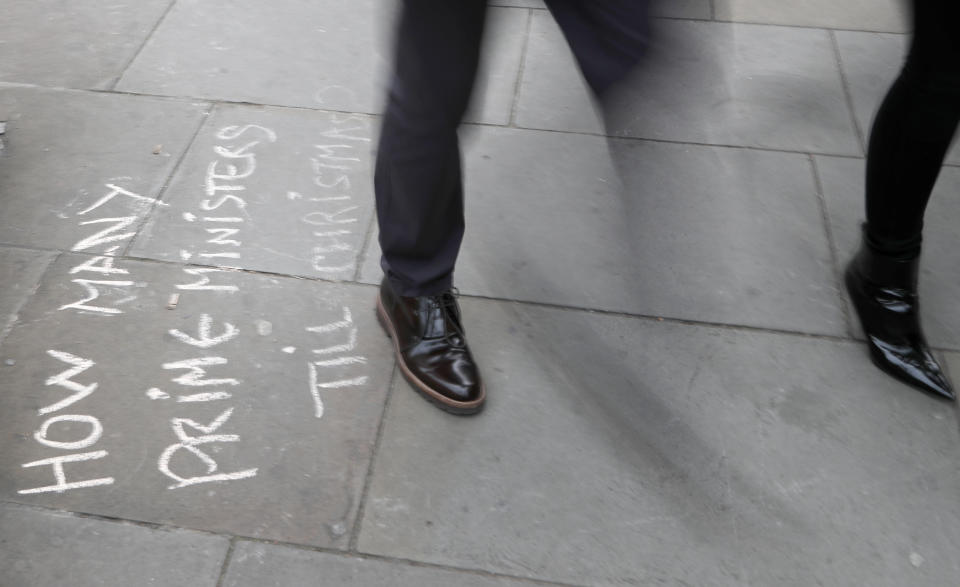 People walk past markings by protestors on the pavement opposite the Houses of Parliament in London, Monday, Sept. 9, 2019. British Prime Minister Boris Johnson voiced optimism Monday that a new Brexit deal can be reached so Britain leaves the European Union by Oct. 31.(AP Photo/Frank Augstein)