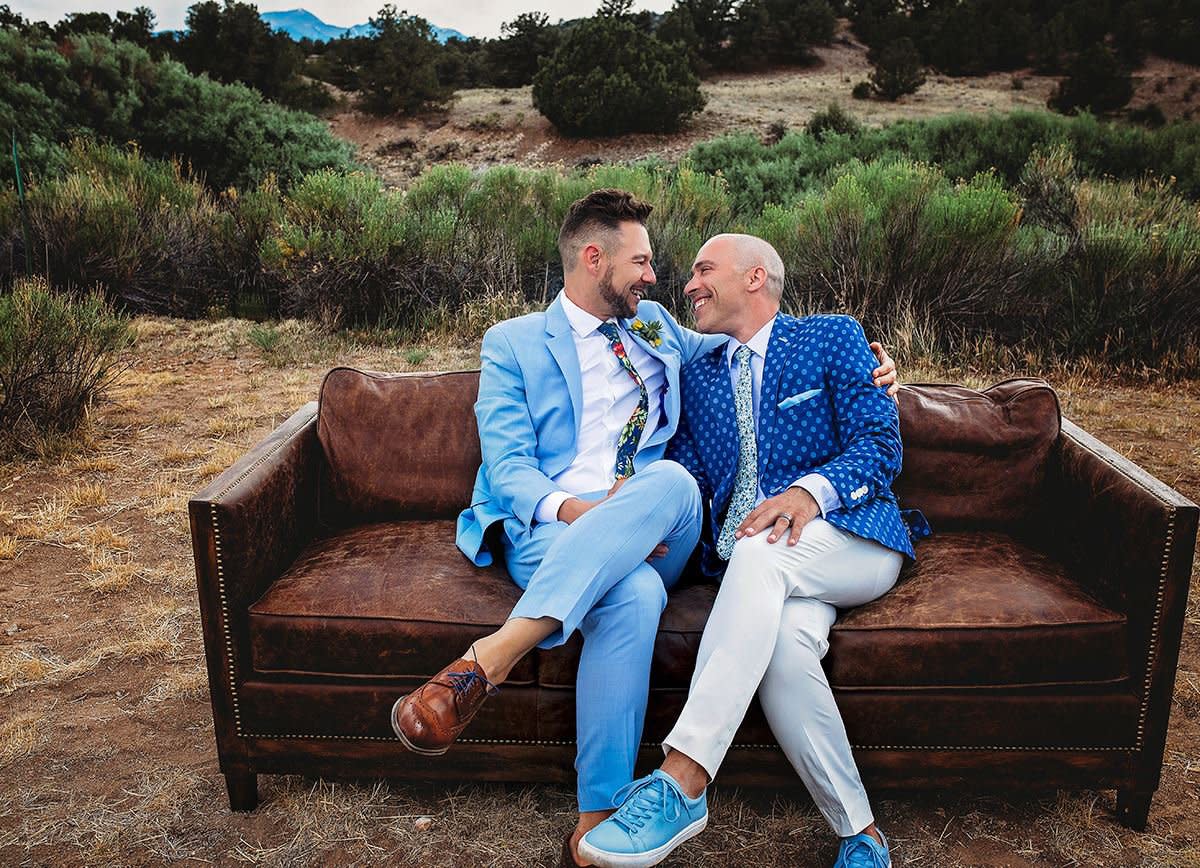 This portrait shows a gay couple sitting on a couch together in the mountains after being married. 