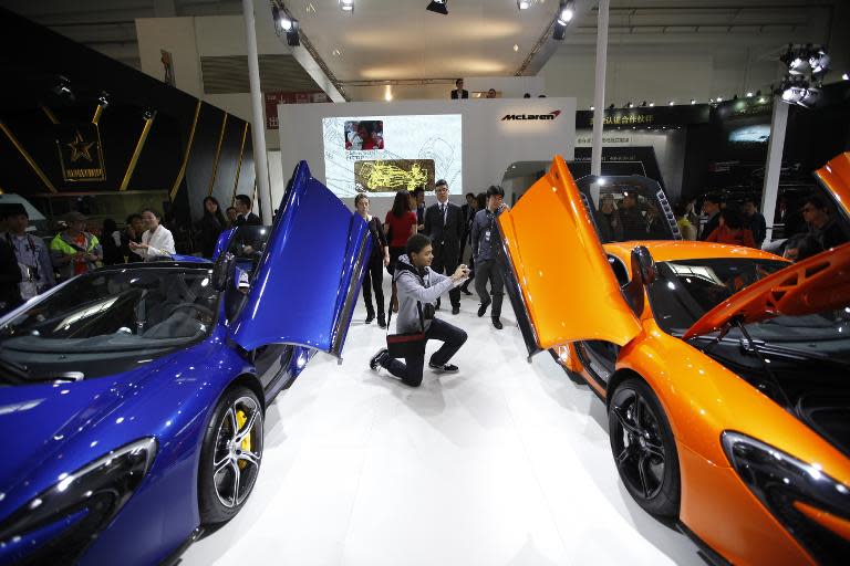 A visitor (C) takes a photo of a Mclaren car on display at the Beijing International Automotive Exhibition on April 20, 2014