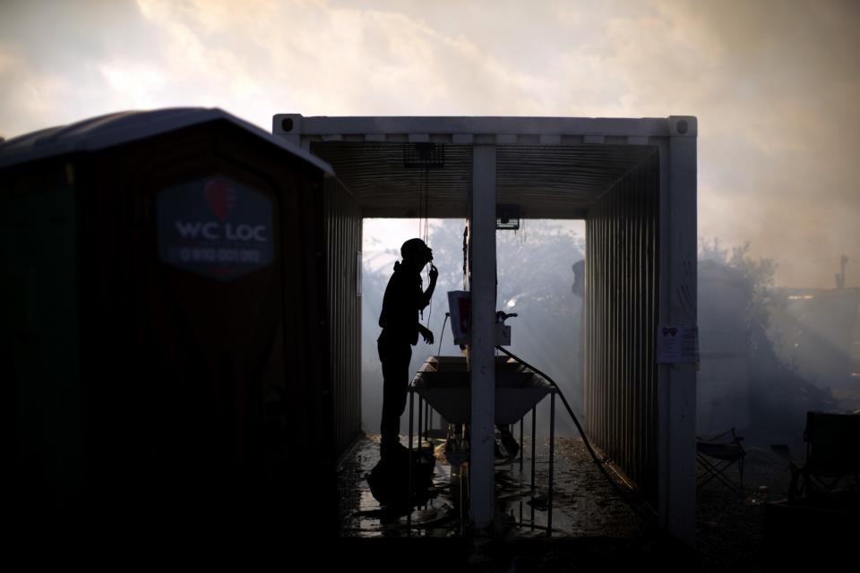 <p>A man shaves himself amid clouds of smoke from burning tents, as workers clean up the makeshift “Jungle” migrant camp near Calais, northern France. (AP Photo/Emilio Morenatti) </p>