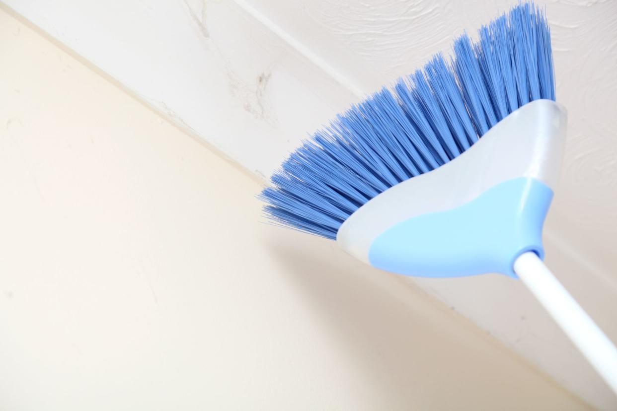 brushing away cobwebs on ceiling - spring cleaning