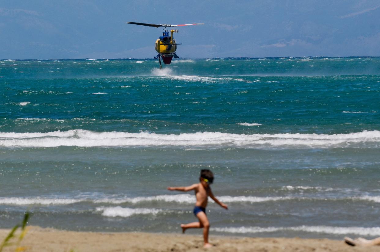 A boy plays on the beachfront as a firefighting helicopter hovers above the sea to refill water for a drop on wildfires near the village of Loutses on the Greek island of Corfu (AFP via Getty Images)