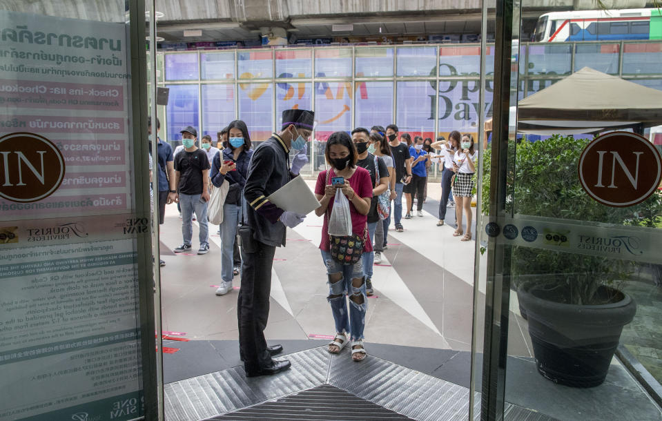 A woman displays her phone to doorman, to conform using a mobile application to help contact-tracing at the entrance to the upmarket shopping mall Siam Paragon in Bangkok, Thailand, Sunday, May 17, 2020. Thai authorities allowed department stores, shopping malls and other businesses to reopen from Sunday, selectively easing restrictions meant to combat the coronavirus. (AP Photo/ Gemunu Amarasinghe)