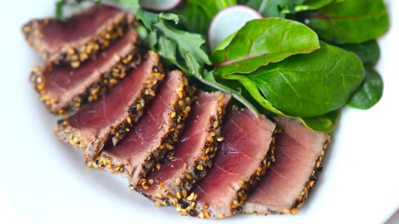 Blush-pink tuna steak on a plate with mixed greens
