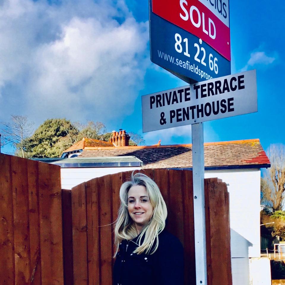 Isabel Oakeshott stands with the 'Sold' sign after buying a top-floor apartment on the Isle of Wight which came with a small seafront terrace