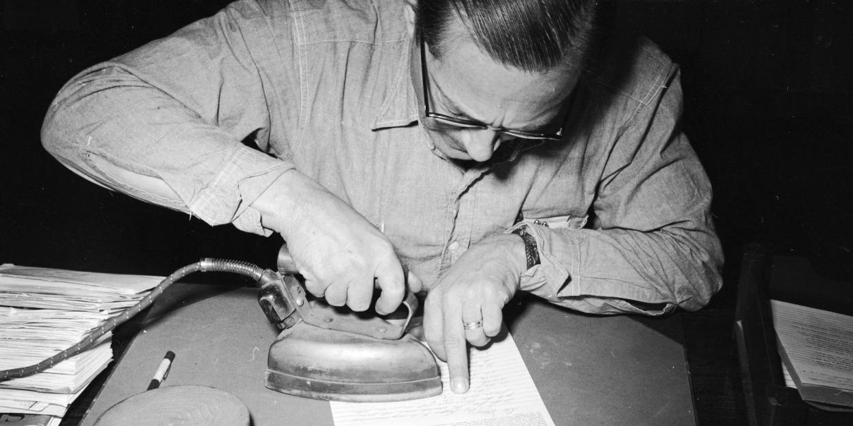 William Abel, a mail censor at Iowa's State Prison, Fort Madison, using a hot iron to bring out a secret message written in lemon juice on a letter.