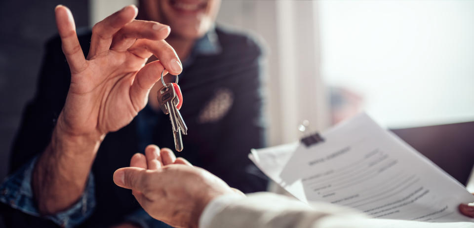 Real estate agent sitting at the desk by the window and passing keys to his client in the office