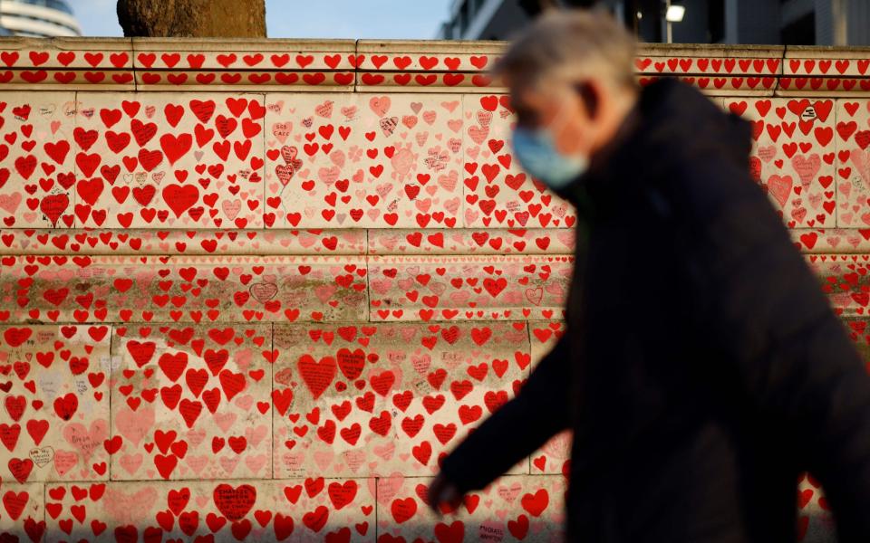 A pedestrian wearing a face mask walks past the National Covid Memorial Wall in London