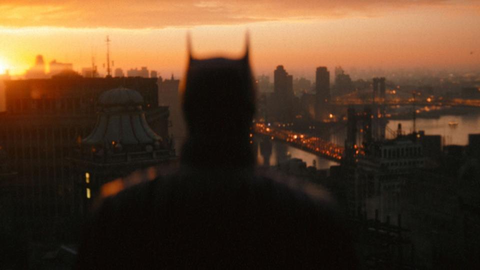 Robert Pattinson's The Batman's silhouette oversees Gotham City at dusk.