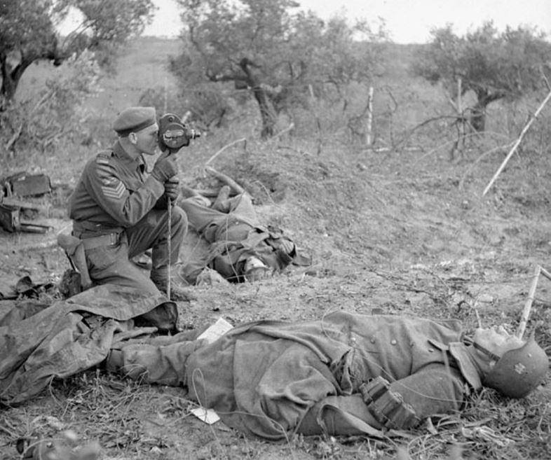 Sgt. George Game films between two German bodies on the outskirts of San Leonardo near Ortona, Dec. 10, 1943. 